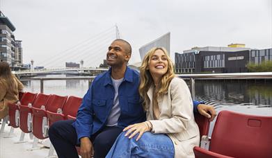 People sat on cruise boat with MediaCity in the background